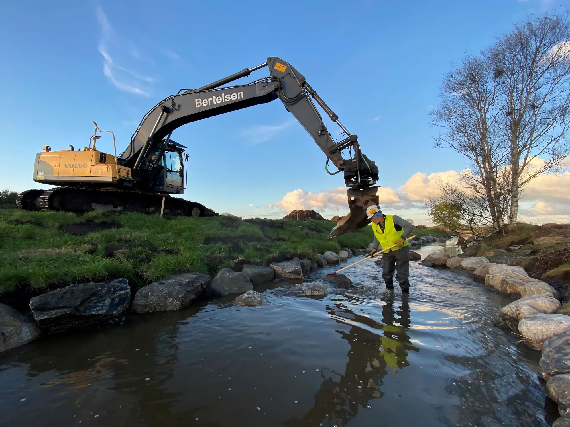 Gravemaskin i arbeid ved bekk